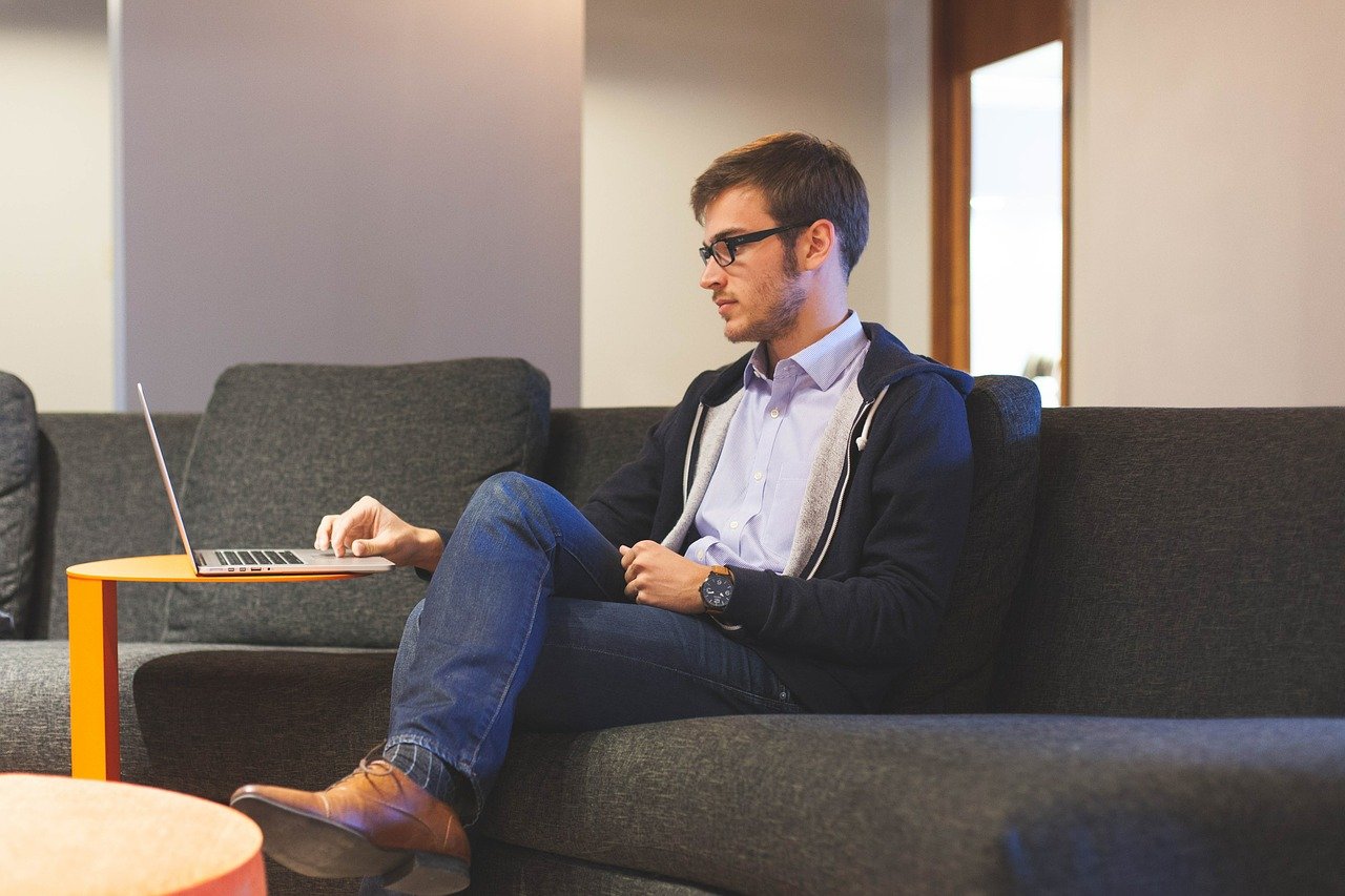 Hombre joven sentado en un sofá, es un ejemplo de las comodidades de tener un trabajo freelance