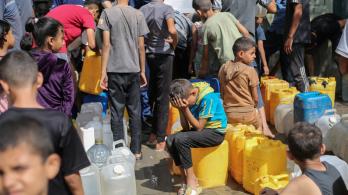 Niños palestinos sentados sobre sus contenedores mientras hacen cola para recibir agua en un punto de distribución benéfico en el campo de refugiados de Nuseirat, en la Franja de Gaza, sitiada por Israel. 