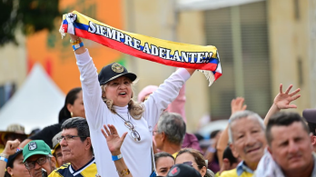 En un evento masivo en plaza pública, una señora levanta una cinta con la bandera de Colombia que dice "siempre adelante"