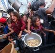 Los palestinos se agolpan para recibir una comida caliente de una cocina benéfica en el campo de refugiados de Nuseirat, en la Franja de Gaza, sitiada por Israel.
