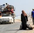 Una mujer camina tirando de un saco con una mano y con la otra de una chapa metálica usada como recipiente para otros objetos, por la carretera costera que usan las personas que huyen hacia el sur desde la ciudad de Gaza, en Nuseirat, en la Franja de Gaza central.