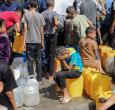 Niños palestinos sentados sobre sus contenedores mientras hacen cola para recibir agua en un punto de distribución benéfico en el campo de refugiados de Nuseirat, en la Franja de Gaza, sitiada por Israel. 