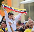 En un evento masivo en plaza pública, una señora levanta una cinta con la bandera de Colombia que dice "siempre adelante"