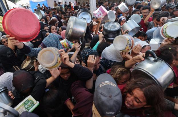 Los palestinos se agolpan para recibir una comida caliente de una cocina benéfica en el campo de refugiados de Nuseirat, en la Franja de Gaza, sitiada por Israel.