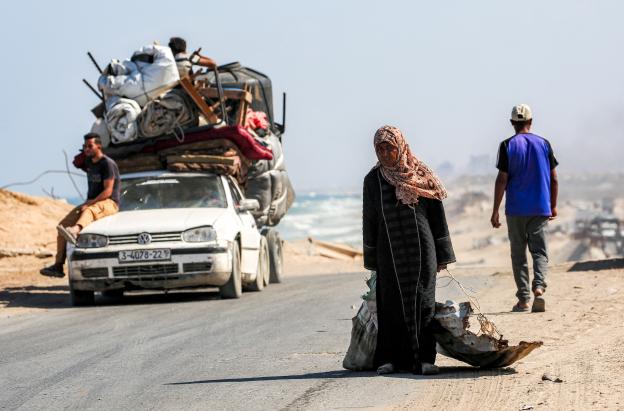 Una mujer camina tirando de un saco con una mano y con la otra de una chapa metálica usada como recipiente para otros objetos, por la carretera costera que usan las personas que huyen hacia el sur desde la ciudad de Gaza, en Nuseirat, en la Franja de Gaza central.