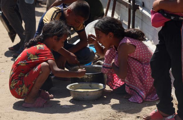 En un comedor social de Jan Yunis, en el sur de la Franja de Gaza, se reparten raciones de comida caliente entre los niños palestinos. Mientras esperan su turno, algunos comen arroz cocido.