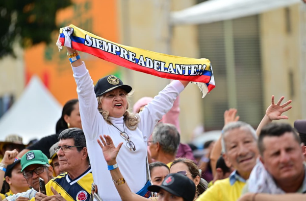 En un evento masivo en plaza pública, una señora levanta una cinta con la bandera de Colombia que dice "siempre adelante"