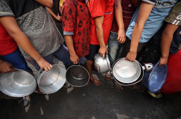 Niños palestinos hacen cola frente a un comedor social en el campo de refugiados de Nuseirat, en el centro de la Franja de Gaza. 