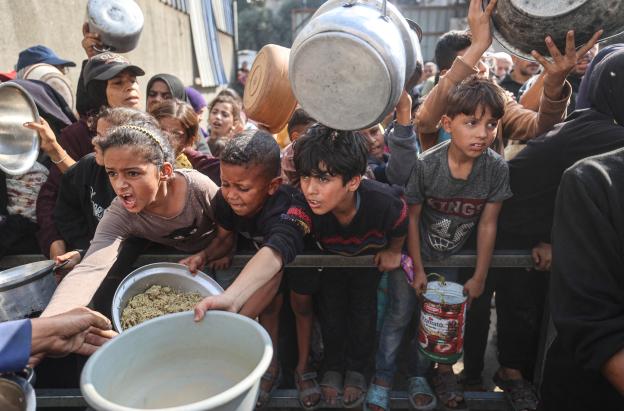 Jóvenes palestinos desplazados esperan con sus recipientes para recibir una ración de comida en el campo de refugiados de Nuseirat, en el centro de la Franja de Gaza, tras hambruna declarada por la ONU en el enclave. 