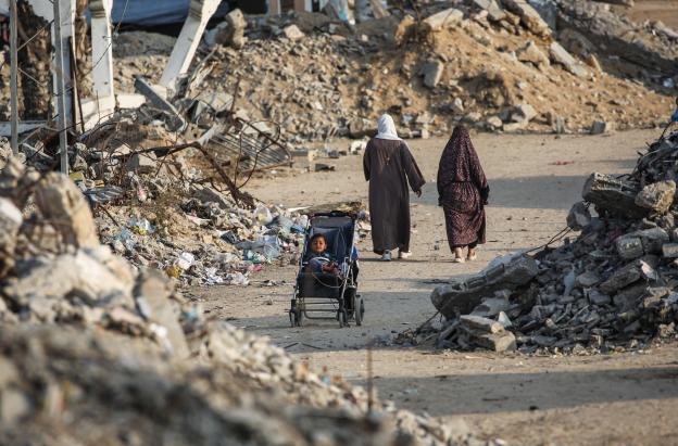 Un niño palestino sentado en un cochecito junto a una carretera destruida en Nuseirat, Franja de Gaza.