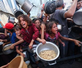 Los palestinos se agolpan para recibir una comida caliente de una cocina benéfica en el campo de refugiados de Nuseirat, en la Franja de Gaza, sitiada por Israel.