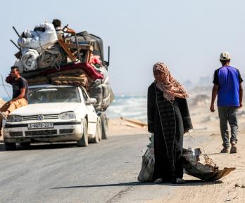 Una mujer camina tirando de un saco con una mano y con la otra de una chapa metálica usada como recipiente para otros objetos, por la carretera costera que usan las personas que huyen hacia el sur desde la ciudad de Gaza, en Nuseirat, en la Franja de Gaza central.