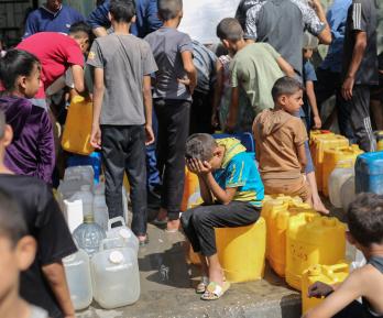 Niños palestinos sentados sobre sus contenedores mientras hacen cola para recibir agua en un punto de distribución benéfico en el campo de refugiados de Nuseirat, en la Franja de Gaza, sitiada por Israel. 