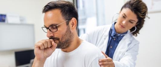 Señor tosiendo muy duro mientras la doctora lo examina