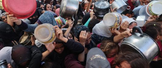 Los palestinos se agolpan para recibir una comida caliente de una cocina benéfica en el campo de refugiados de Nuseirat, en la Franja de Gaza, sitiada por Israel.