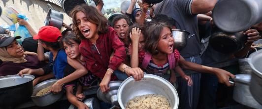 Los palestinos se agolpan para recibir una comida caliente de una cocina benéfica en el campo de refugiados de Nuseirat, en la Franja de Gaza, sitiada por Israel.