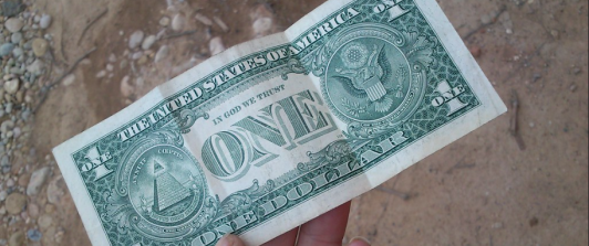 billete de un dólar sostenido por una mano, fondo piso de tierra 