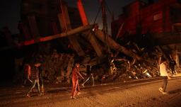 Palestinos pasan junto a un edificio destruido en el campo de refugiados de Al-Bureij, en el centro de la Franja de Gaza, durante la noche.