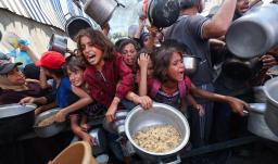 Los palestinos se agolpan para recibir una comida caliente de una cocina benéfica en el campo de refugiados de Nuseirat, en la Franja de Gaza, sitiada por Israel.