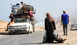 Una mujer camina tirando de un saco con una mano y con la otra de una chapa metálica usada como recipiente para otros objetos, por la carretera costera que usan las personas que huyen hacia el sur desde la ciudad de Gaza, en Nuseirat, en la Franja de Gaza central.