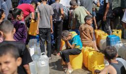 Niños palestinos sentados sobre sus contenedores mientras hacen cola para recibir agua en un punto de distribución benéfico en el campo de refugiados de Nuseirat, en la Franja de Gaza, sitiada por Israel. 