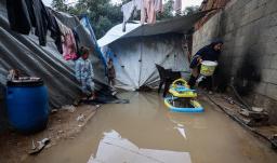 Los niños miran a una mujer que lleva un cubo después de que las fuertes lluvias inundaran un campamento improvisado que alberga a palestinos desplazados en el campo de refugiados de Maghazi, en el centro de la Franja de Gaza.