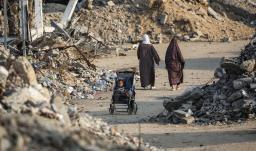 Un niño palestino sentado en un cochecito junto a una carretera destruida en Nuseirat, Franja de Gaza.