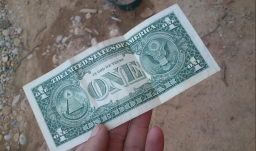 billete de un dólar sostenido por una mano, fondo piso de tierra 