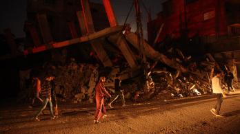 Palestinos pasan junto a un edificio destruido en el campo de refugiados de Al-Bureij, en el centro de la Franja de Gaza, durante la noche.