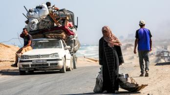 Una mujer camina tirando de un saco con una mano y con la otra de una chapa metálica usada como recipiente para otros objetos, por la carretera costera que usan las personas que huyen hacia el sur desde la ciudad de Gaza, en Nuseirat, en la Franja de Gaza central.