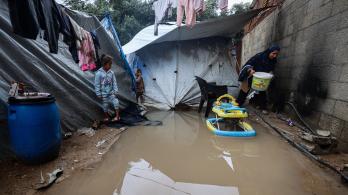 Los niños miran a una mujer que lleva un cubo después de que las fuertes lluvias inundaran un campamento improvisado que alberga a palestinos desplazados en el campo de refugiados de Maghazi, en el centro de la Franja de Gaza.