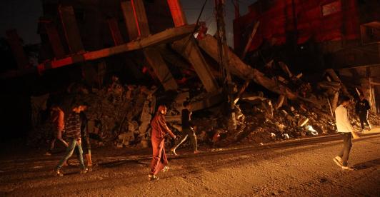 Palestinos pasan junto a un edificio destruido en el campo de refugiados de Al-Bureij, en el centro de la Franja de Gaza, durante la noche.