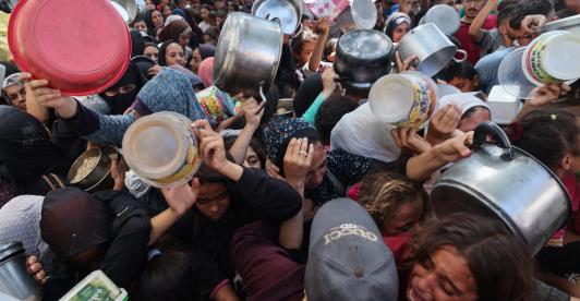 Los palestinos se agolpan para recibir una comida caliente de una cocina benéfica en el campo de refugiados de Nuseirat, en la Franja de Gaza, sitiada por Israel.