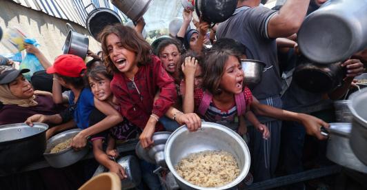 Los palestinos se agolpan para recibir una comida caliente de una cocina benéfica en el campo de refugiados de Nuseirat, en la Franja de Gaza, sitiada por Israel.