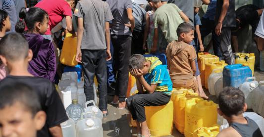 Niños palestinos sentados sobre sus contenedores mientras hacen cola para recibir agua en un punto de distribución benéfico en el campo de refugiados de Nuseirat, en la Franja de Gaza, sitiada por Israel. 