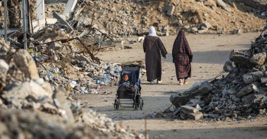Un niño palestino sentado en un cochecito junto a una carretera destruida en Nuseirat, Franja de Gaza.
