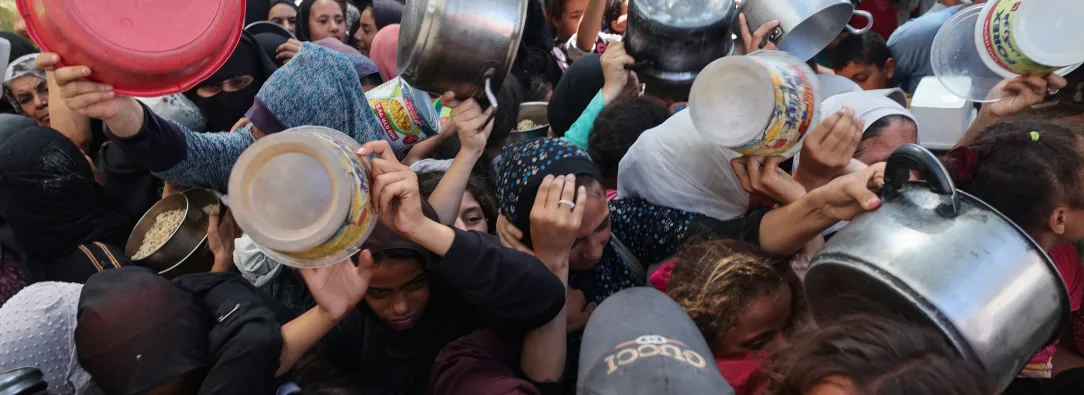 Los palestinos se agolpan para recibir una comida caliente de una cocina benéfica en el campo de refugiados de Nuseirat, en la Franja de Gaza, sitiada por Israel.