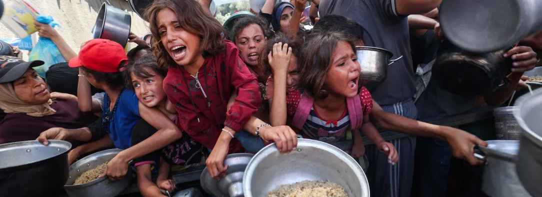 Los palestinos se agolpan para recibir una comida caliente de una cocina benéfica en el campo de refugiados de Nuseirat, en la Franja de Gaza, sitiada por Israel.