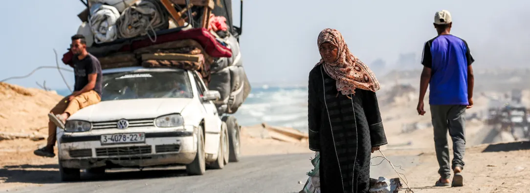 Una mujer camina tirando de un saco con una mano y con la otra de una chapa metálica usada como recipiente para otros objetos, por la carretera costera que usan las personas que huyen hacia el sur desde la ciudad de Gaza, en Nuseirat, en la Franja de Gaza central.