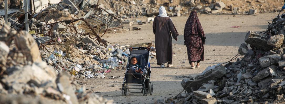 Un niño palestino sentado en un cochecito junto a una carretera destruida en Nuseirat, Franja de Gaza.