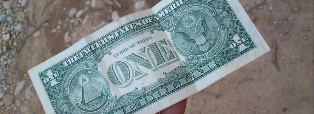 billete de un dólar sostenido por una mano, fondo piso de tierra 