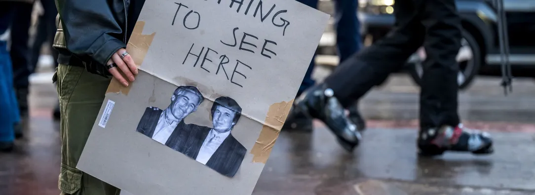 Un manifestante sostiene una pancarta con fotografías de Jeffrey Epstein (izquierda), un acaudalado financiero estadounidense que murió en prisión en 2019 mientras esperaba juicio por tráfico sexual de menores, y del presidente de Estados Unidos, Donald Trump (derecha), durante una manifestación contra el Foro Económico Mundial (FEM) en vísperas de la reunión anual del FEM en Davos.