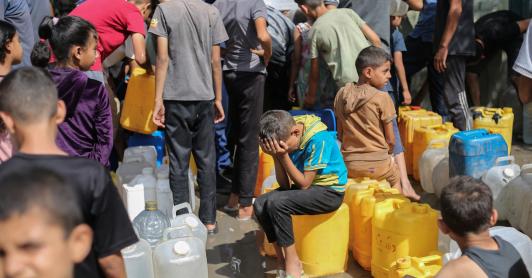 Niños palestinos sentados sobre sus contenedores mientras hacen cola para recibir agua en un punto de distribución benéfico en el campo de refugiados de Nuseirat, en la Franja de Gaza, sitiada por Israel. 