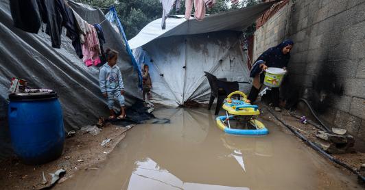 Los niños miran a una mujer que lleva un cubo después de que las fuertes lluvias inundaran un campamento improvisado que alberga a palestinos desplazados en el campo de refugiados de Maghazi, en el centro de la Franja de Gaza.