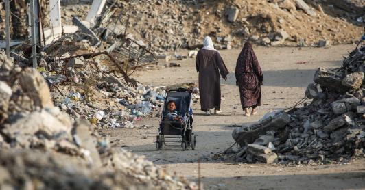 Un niño palestino sentado en un cochecito junto a una carretera destruida en Nuseirat, Franja de Gaza.